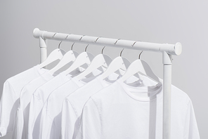 collection of trendy white t-shirts hanging on clothes rack isolated on grey