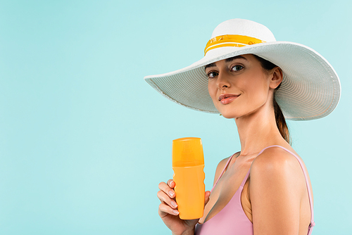 pretty woman in sun hat holding bottle of sunscreen isolated on blue