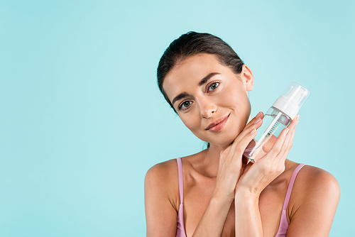 pretty woman holding bottle of face tonic while smiling isolated on blue
