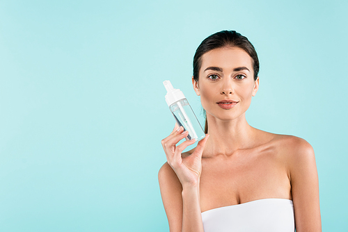 brunette woman in white strapless top showing face tonic isolated on blue