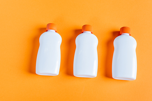 top view of white bottles with sunscreen on orange background