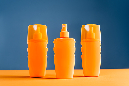 spray bottles of sunblock on orange surface isolated on blue