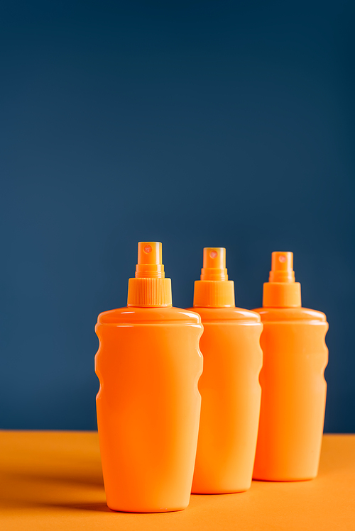 spray bottles with sunblock on orange surface isolated on blue