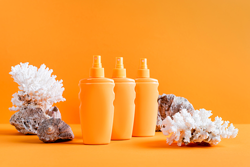 spray bottles of sunscreen near sea corals isolated on orange