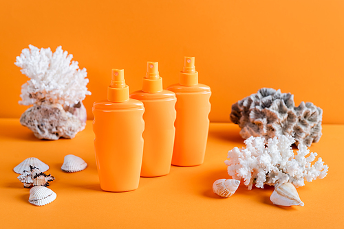sea corals and bottles with sunscreen on orange background