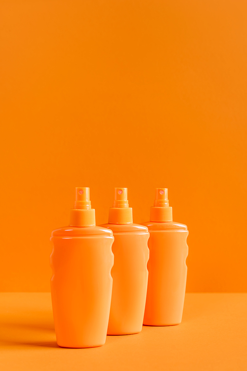 spray bottles of sunscreen isolated on orange