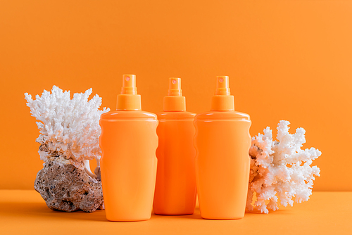 containers with sunblock near sea corals isolated on orange