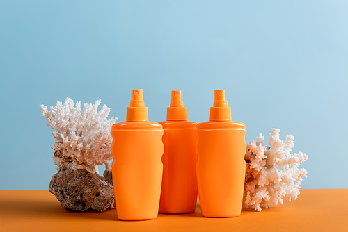 orange bottles of sunscreen near sea corals isolated on blue