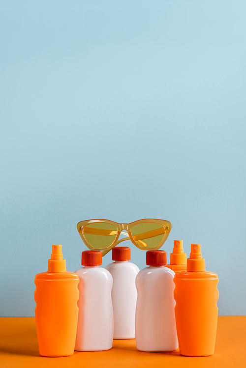white and orange bottles of sunblock and sunglasses isolated on blue