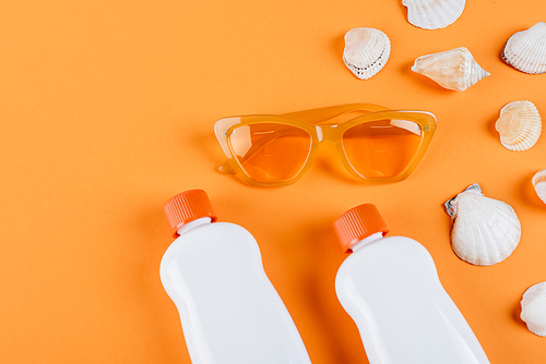 top view of sunglasses, white sunscreen bottles and seashells on orange surface