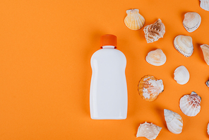 top view of seashells near white bottle of sunblock on orange surface