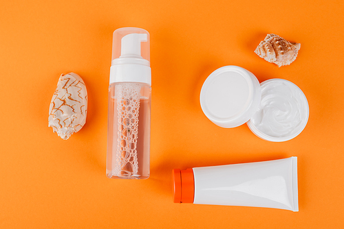top view of containers with cosmetic cream, face tonic and sunscreen near seashells on orange