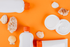 top view of seashells near containers with sunblock and cosmetic cream on orange