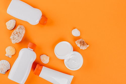 top view of containers with sunblock near cosmetic cream and seashells on orange