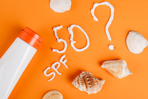 top view of sunscreen near seashells, spf lettering and number fifty with question mark on orange surface