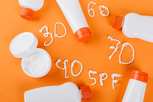 top view of sunscreen and cosmetic cream near different numbers and spf lettering on orange