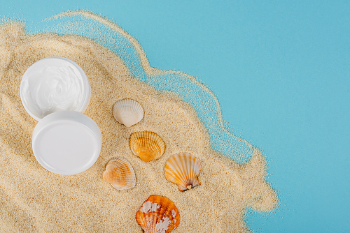 top view of seashells near cosmetic cream on sand and blue surface