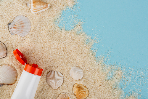 top view of tube of sunblock and seashells on sand and blue surface
