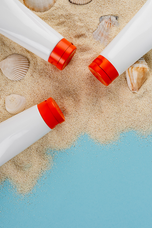 top view of seashells and tubes with sunblock on sand and blue surface