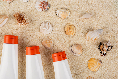 top view of white tubes with sunblock near seashells on sand