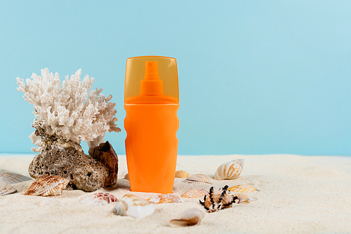 orange bottle of sunscreen near seashells and sea coral on sand isolated on blue