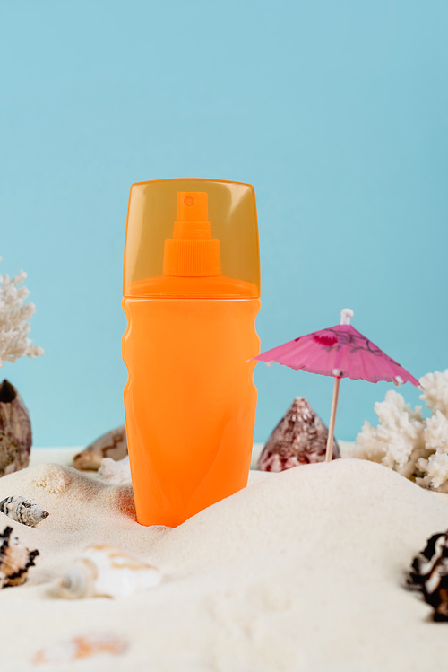 orange spray bottle of sunblock near seashells on sand isolated on blue