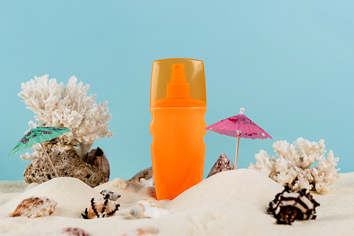 orange bottle of sunscreen near seashells on sand isolated on blue