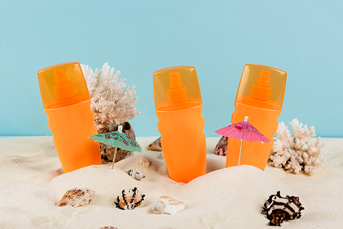 orange bottles of sunblock near seashells on sand isolated on blue