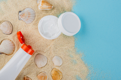 top view of cosmetic cream and sunscreen near seashells on sand and blue surface