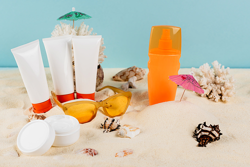 cosmetic cream, sunblock tubes, seashells and sunglasses on sand isolated on blue