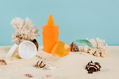 cosmetic cream and bottle of sunscreen near seashells on sand isolated on blue