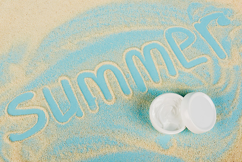 top view of summer lettering made of sand near cosmetic cream on blue surface