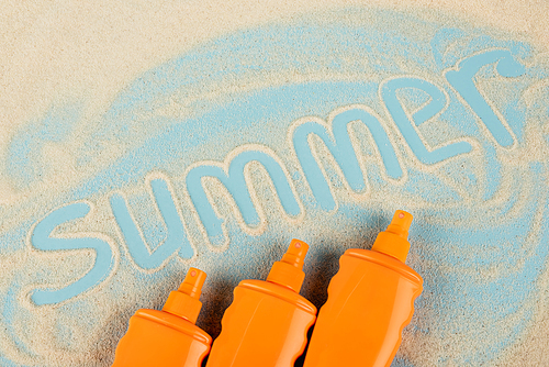 top view of orange bottles with sunblock near summer lettering on sand and blue surface