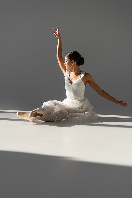 Side view of elegant ballerina sitting on grey background