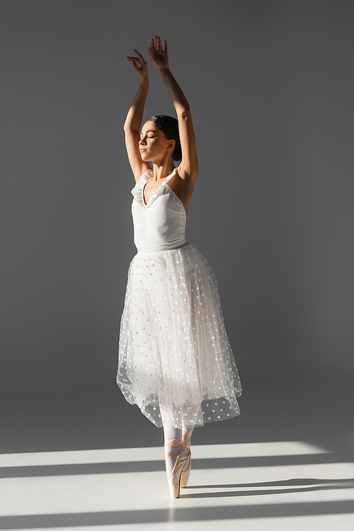 Ballerina dancing with closed eyes on grey background