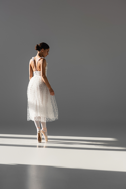 Side view of ballerina in white dress dancing on grey background