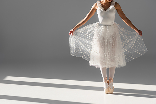 Cropped view of ballerina holding skirt on grey background