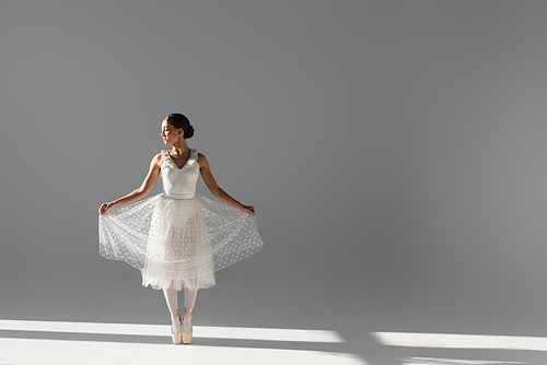 Side view of ballerina holding skirt on grey background