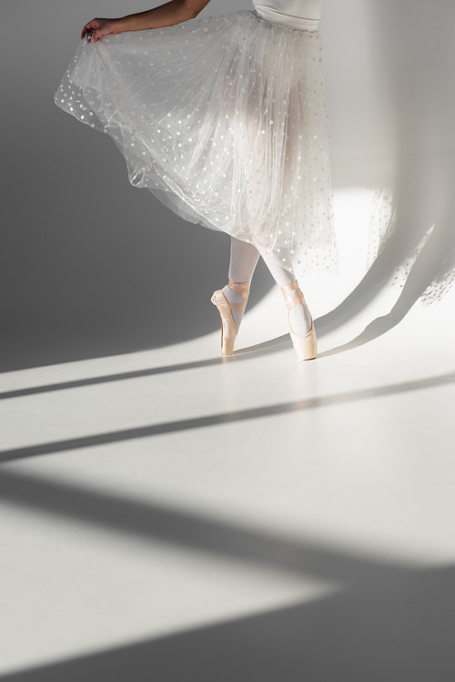 Cropped view of ballerina in white skirt dancing on grey background