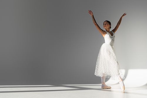 Young ballerina in white dress dancing on grey background