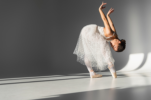 Side view of ballerina bending on grey background