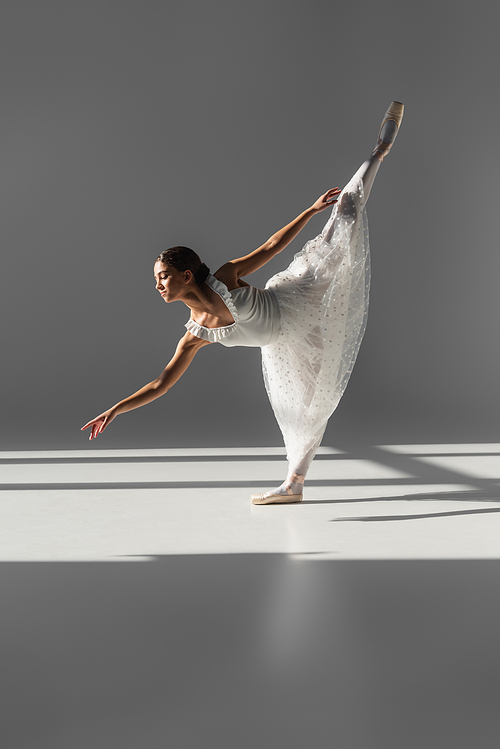 Side view of ballerina standing on one leg on grey background