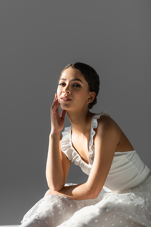 Young ballerina smiling at camera on grey background