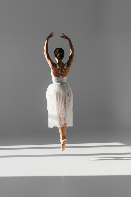 Back view of ballerina dancing on grey background with shadow