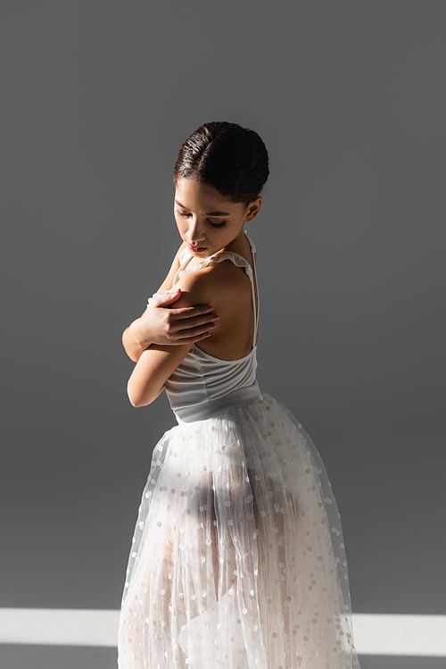 Classical dancer looking at shoulder on grey background with sunlight