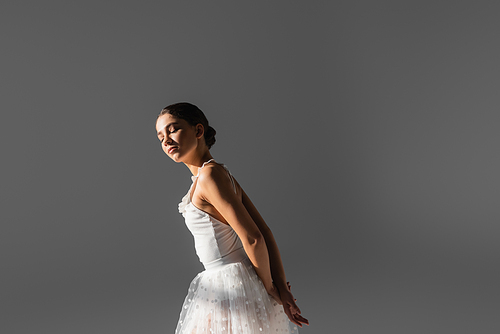 Young ballerina standing in sunlight isolated on grey