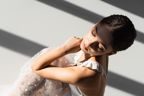 Overhead view of pretty ballerina sitting on grey background with sunlight and shadow