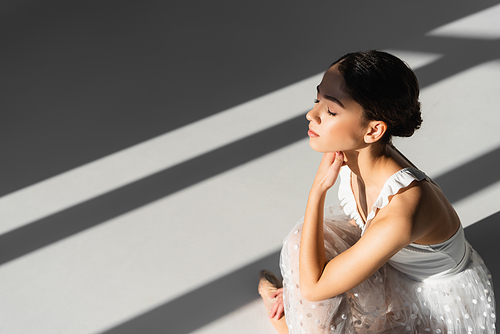 Professional ballerina sitting on grey background with sunlight