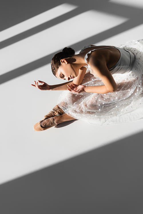 High angle view of ballerina with closed eye dancing on floor on grey background with sunlight