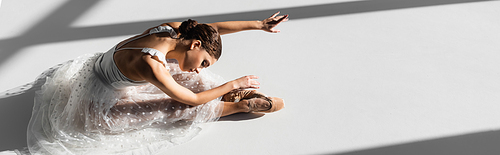 High angle view of ballerina in pointe shoes bending on grey background with sunlight, banner